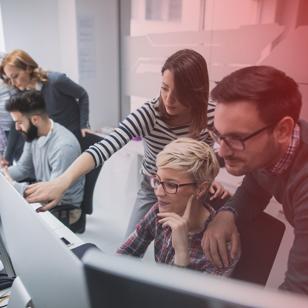 group of three coworkers behind a computer looking at the screen