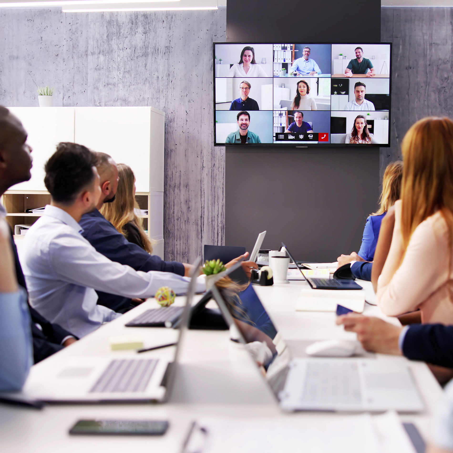 A team of people in an office alongside the at-home team showing a hybrid office